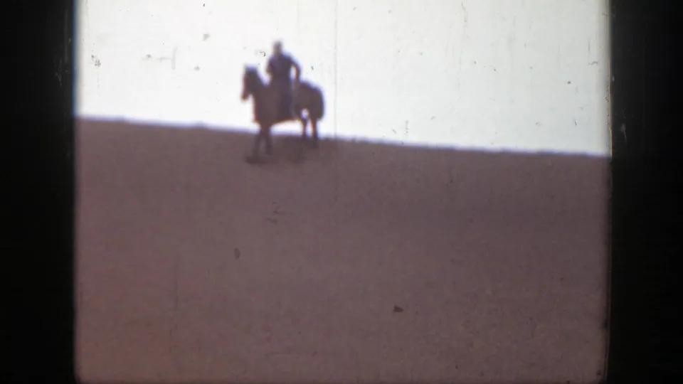 A 1939 Montana home-movie frame shows a mounted rider near the ridge line, with another horse partly visible at left.