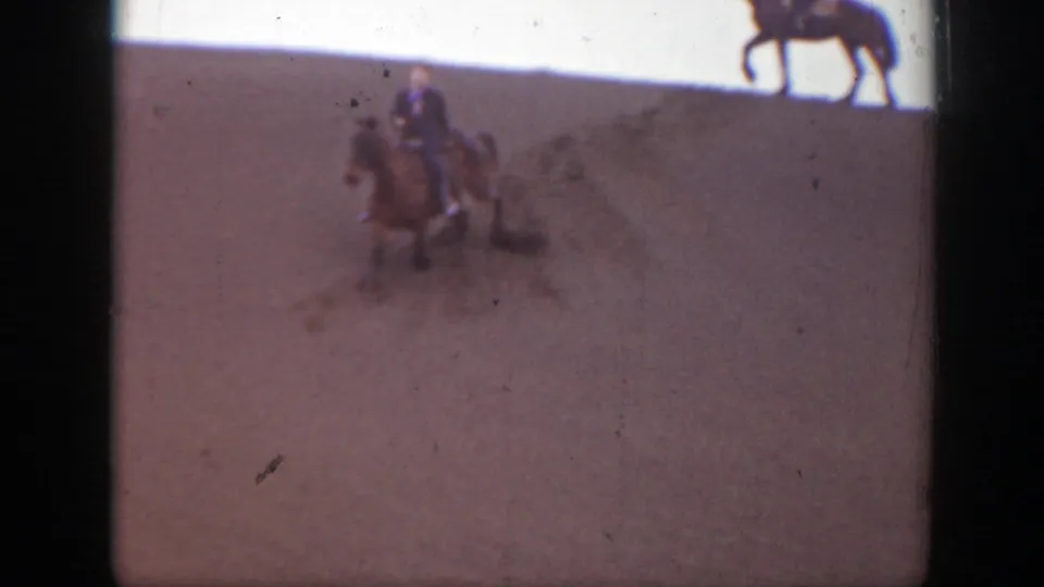 A rider on horseback descends the sandy Montana slope as another horse is partially visible near the top edge of the frame.