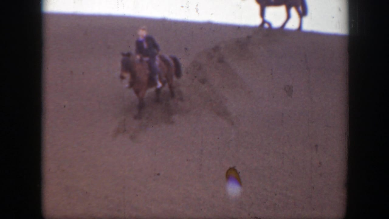 Rider on horseback moving across sandy ground with another horse partly visible above the frame.