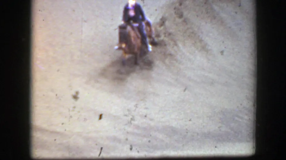 A rider in a blue jacket continues toward the camera on horseback across sandy terrain, recorded on grainy 1939 Montana 8mm film.