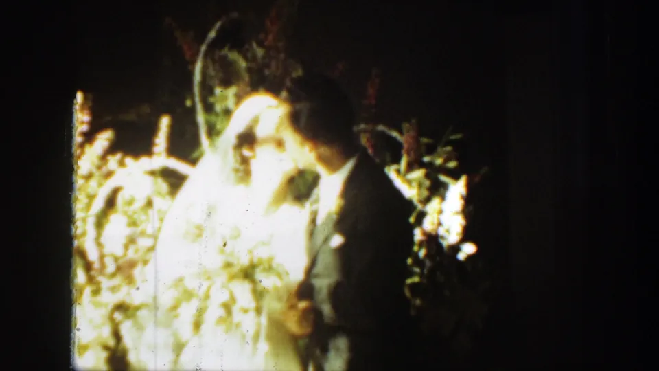 1939 Montana 8mm frame showing the groom kissing the bride while she stands in a white veil beside bright flowers.