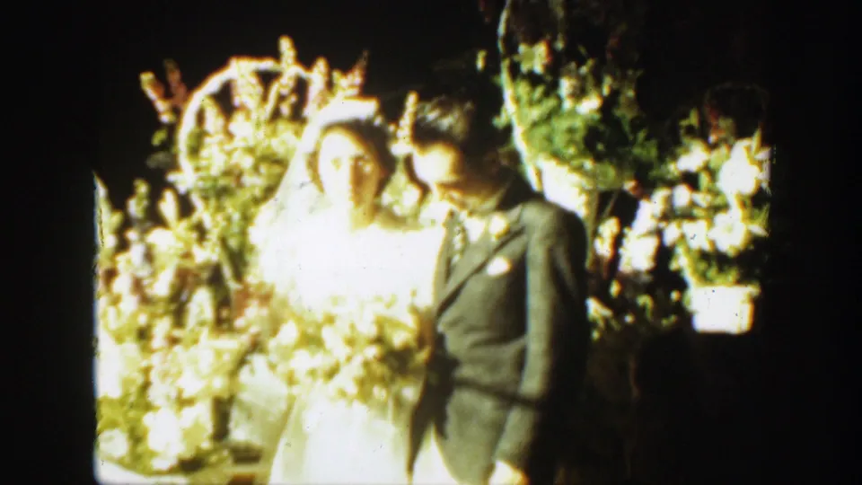 Bride in a white veil and groom in a dark suit stand together before floral displays in the Montana wedding footage.