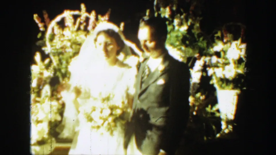 The bride and groom remain beside each other in the 1939 Montana wedding scene, with flowers and greenery behind them.