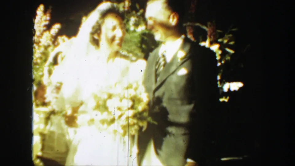 The bride, overexposed by sunlight, turns toward the groom while holding her bouquet in the Montana wedding home movie.