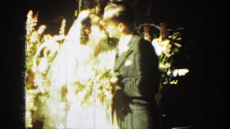 1939 Montana home-movie frame of the bride and groom kissing during an outdoor wedding portrait moment.