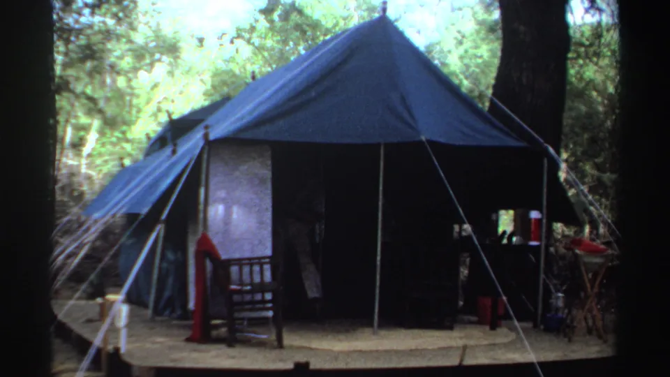 1969 Sudan 8mm frame showing a large blue campsite tent under trees, with chairs and small camp items visible nearby.