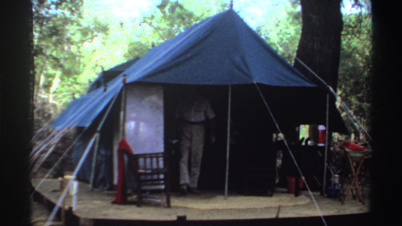 Blue canvas tent on a wooded campsite with a person partly visible in the doorway.