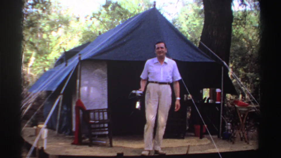 1969 Sudan 8mm frame showing an adult man walking toward the filmer from a blue canvas tent, camera in hand.