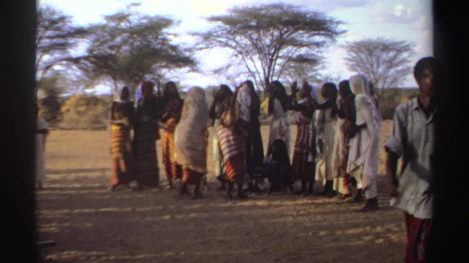 1969 Sudan frame showing women in traditional-looking garments gathered outside, with an observer partly visible at the right edge.