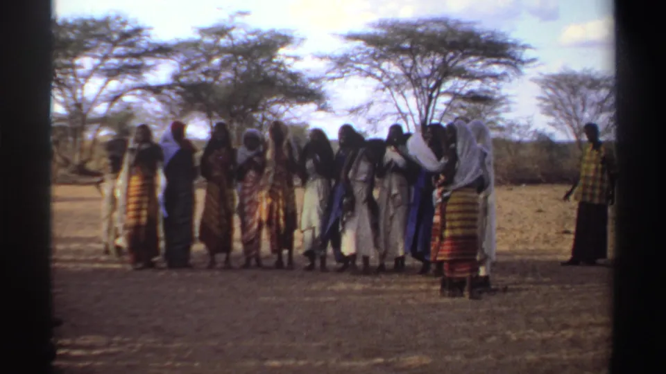 1969 Sudan home-movie frame of women in long dresses and scarves grouped outdoors under sparse trees.