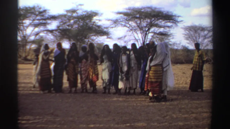 Sudan 1969 8mm still of women gathered outdoors, with patterned garments, pale headscarves, and acacia-like trees behind them.
