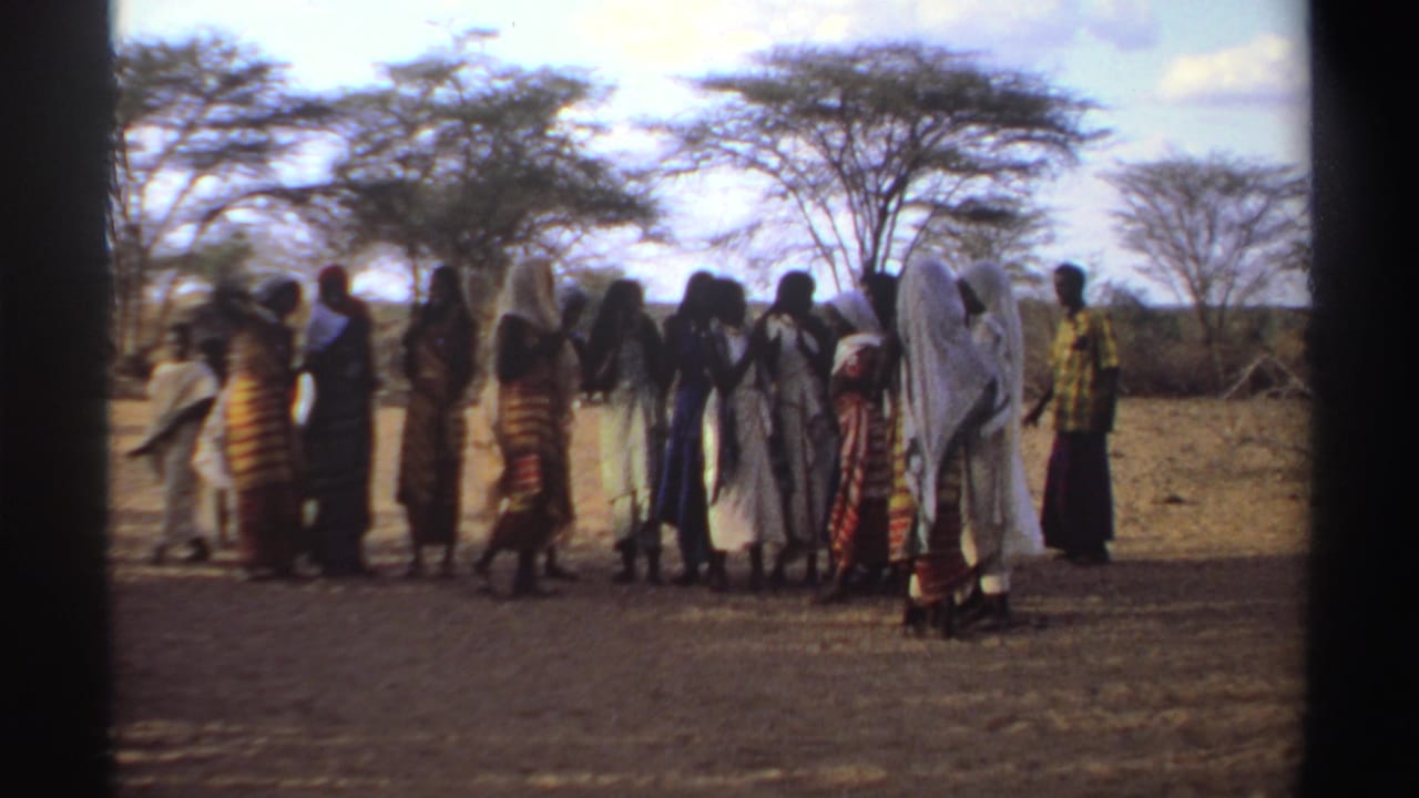 Women stand in a line as a person moves across the foreground.