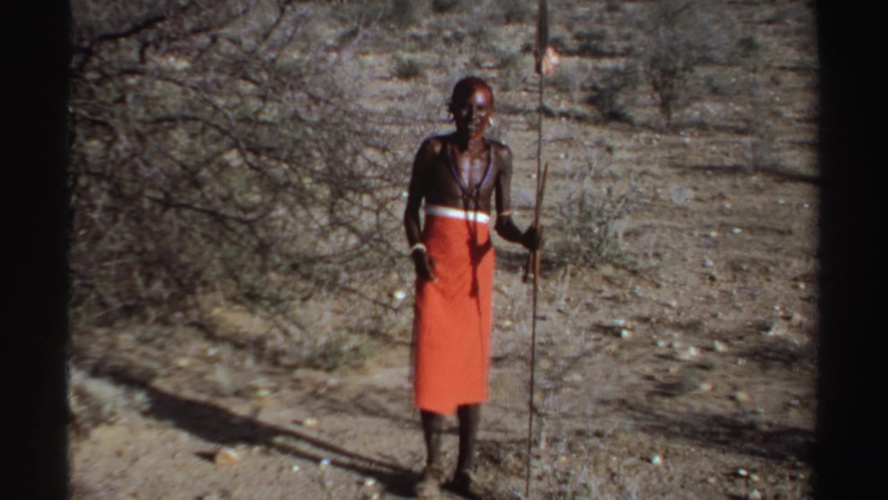 1969 Sudan 8mm frame of a man in orange shuka-style cloth holding a long spear in dry scrubland.