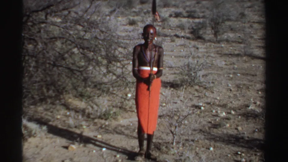1969 Sudan 8mm frame showing a smiling man in orange shuka-style cloth with necklaces and a spear.