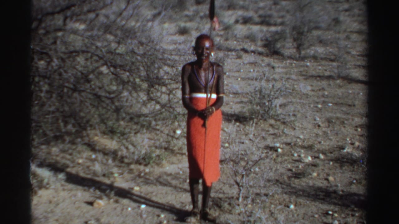 Lone man in red wrapped cloth standing with a spear on dry ground.