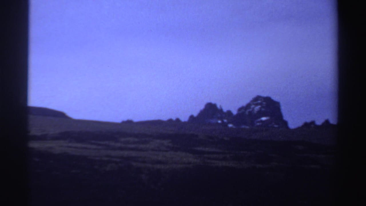 Distant rugged rock formations under a purple-blue sky with dark foreground slopes.