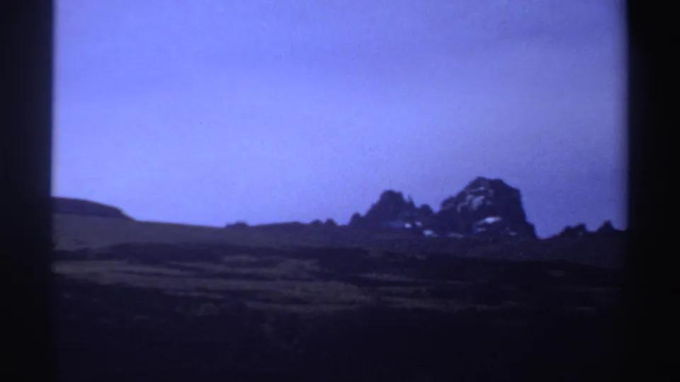 1969 8mm Sudan footage showing distant jagged rock formations beyond dark terrain under a strong purple-blue color cast.