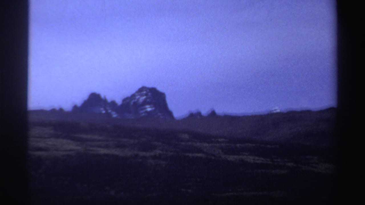 1969 8mm Sudan frame with jagged distant rock forms, pale snow-like markings, and a dark open foreground.