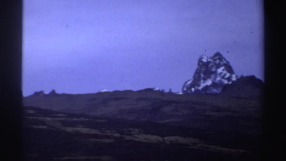 1969 8mm Sudan footage showing a prominent rugged formation with pale snow-like patches above dark rolling terrain.