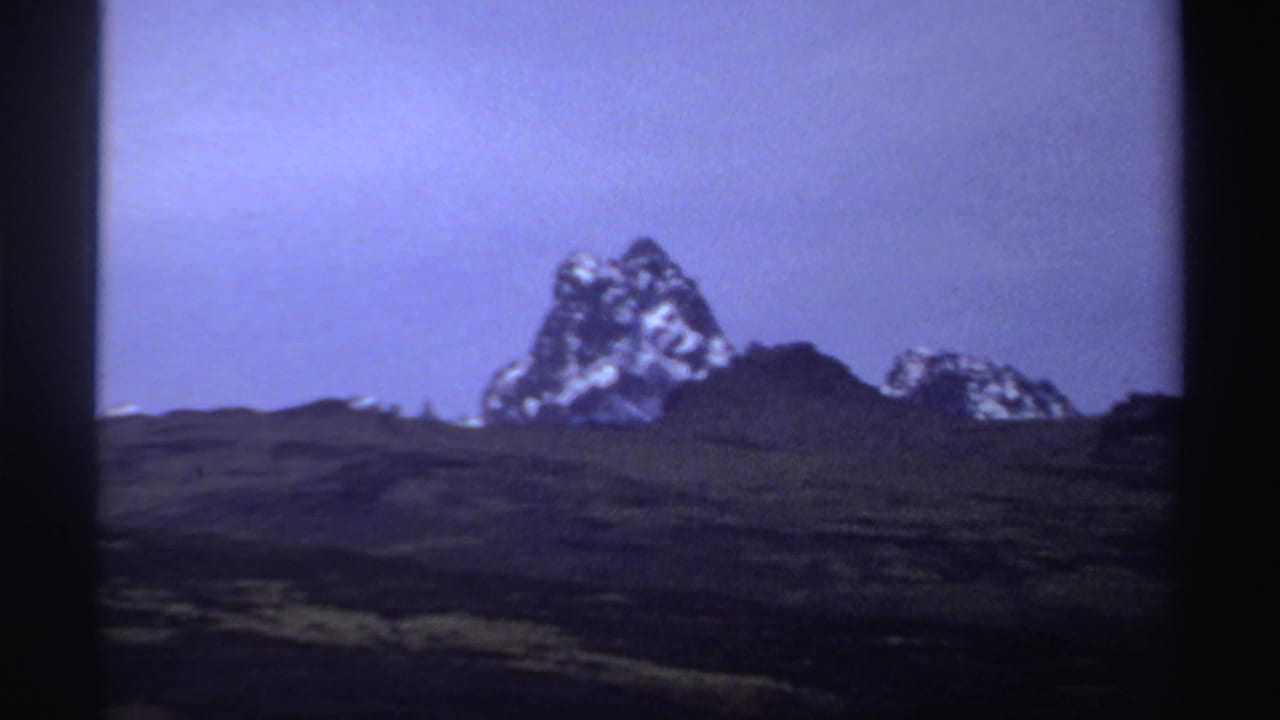 Jagged mountain summit and lower rocky ridge seen across dark terrain.