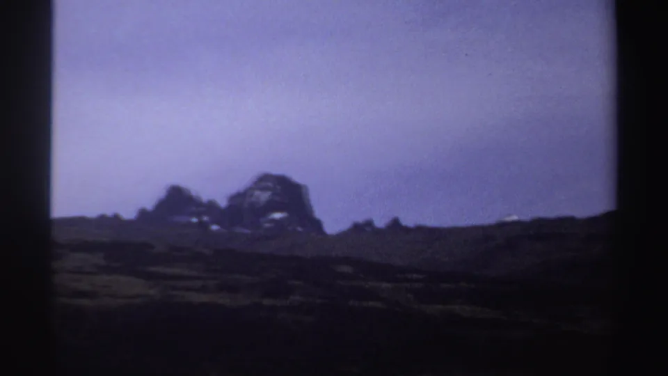 1969 Sudan metadata frame with distant rocky cliffs, small snow patches, dark ridgelines, and a muted pale sky.