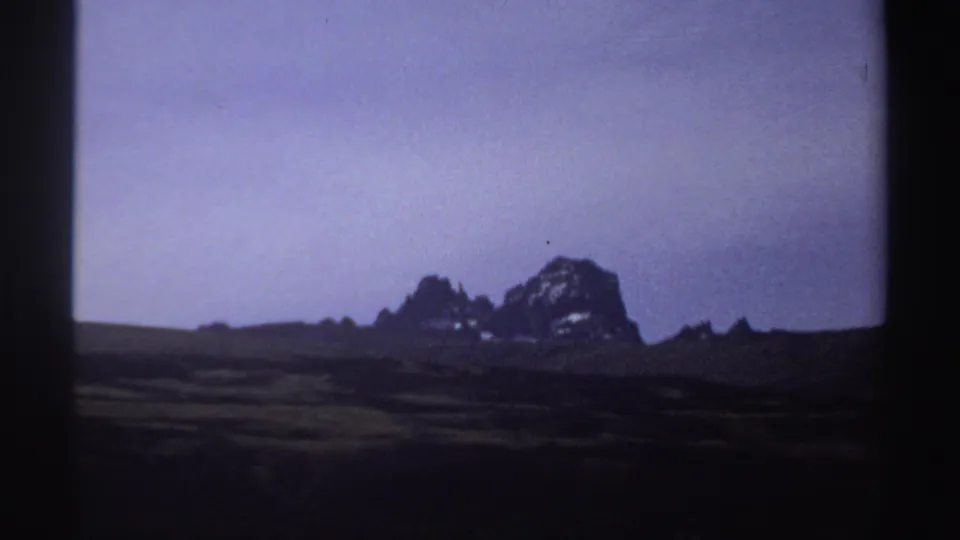1969 Sudan 8mm frame showing a silhouetted rocky ridge and dark foreground under a purple-blue sky.