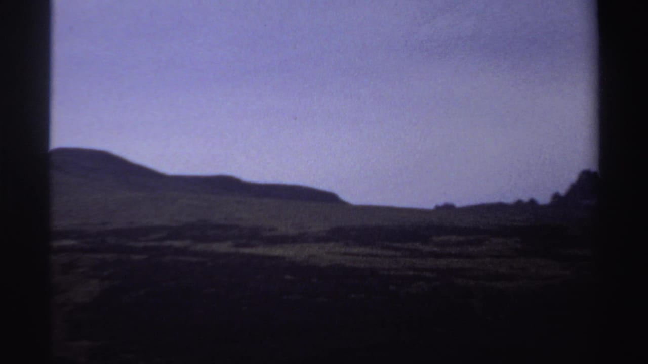 1969 Sudan 8mm frame with a broad rounded hillside, shadowed valley, and muted purple twilight sky.