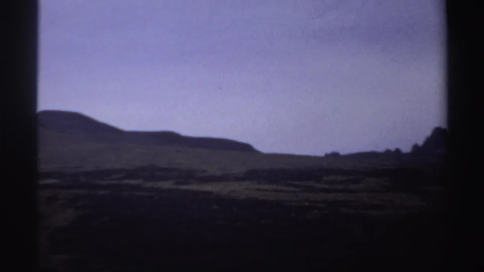 1969 Sudan 8mm frame with a broad rounded hillside, shadowed valley, and muted purple twilight sky.