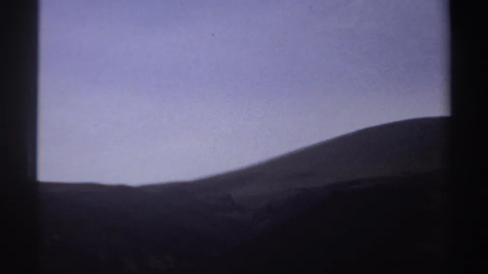 1969 Sudan 8mm frame with a shadowed valley gap, sloping hills, and a pale purple-blue twilight sky.