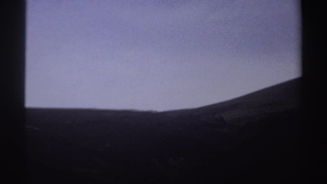 Dark hillside silhouette below a pale sky in soft 8mm exposure.
