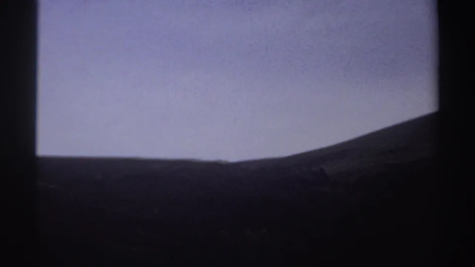 1969 Sudan 8mm frame showing a dark sloped hillside silhouetted against a pale sky, with soft exposure and visible film grain.