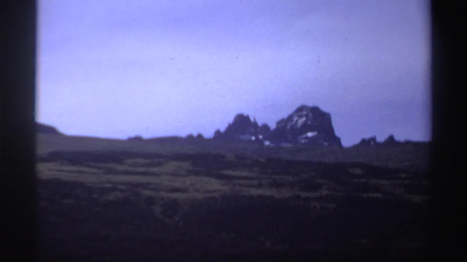 Soft 8mm view of a Sudan landscape in 1969, with dark foreground vegetation and rocky mountain forms on the horizon.