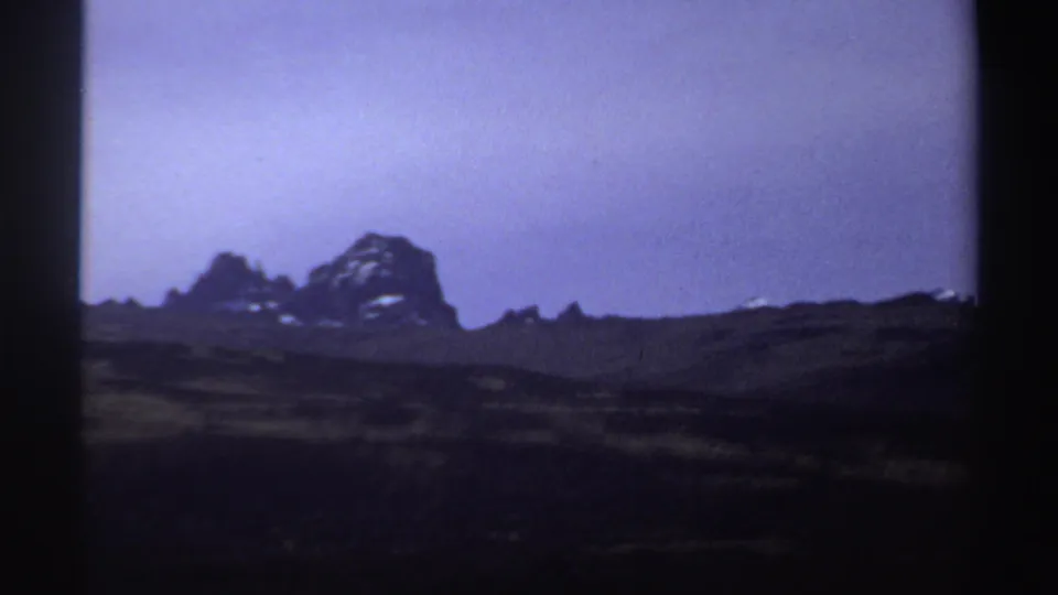 A 1969 Sudan landscape frame shows rough dark ground and distant rocky peaks, softened by exposure and 8mm grain.