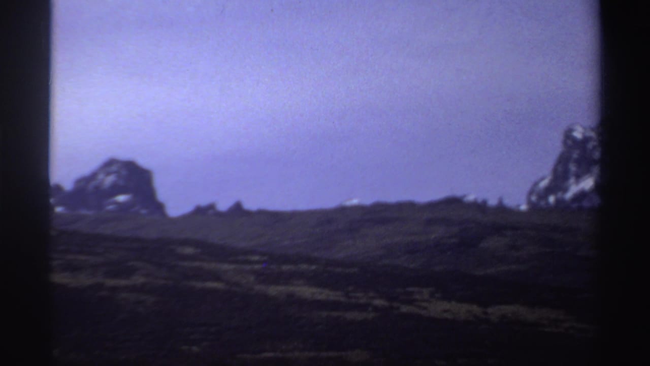1969 Sudan 8mm frame showing a grassy open landscape with distant rocky hills and a purple-blue sky.
