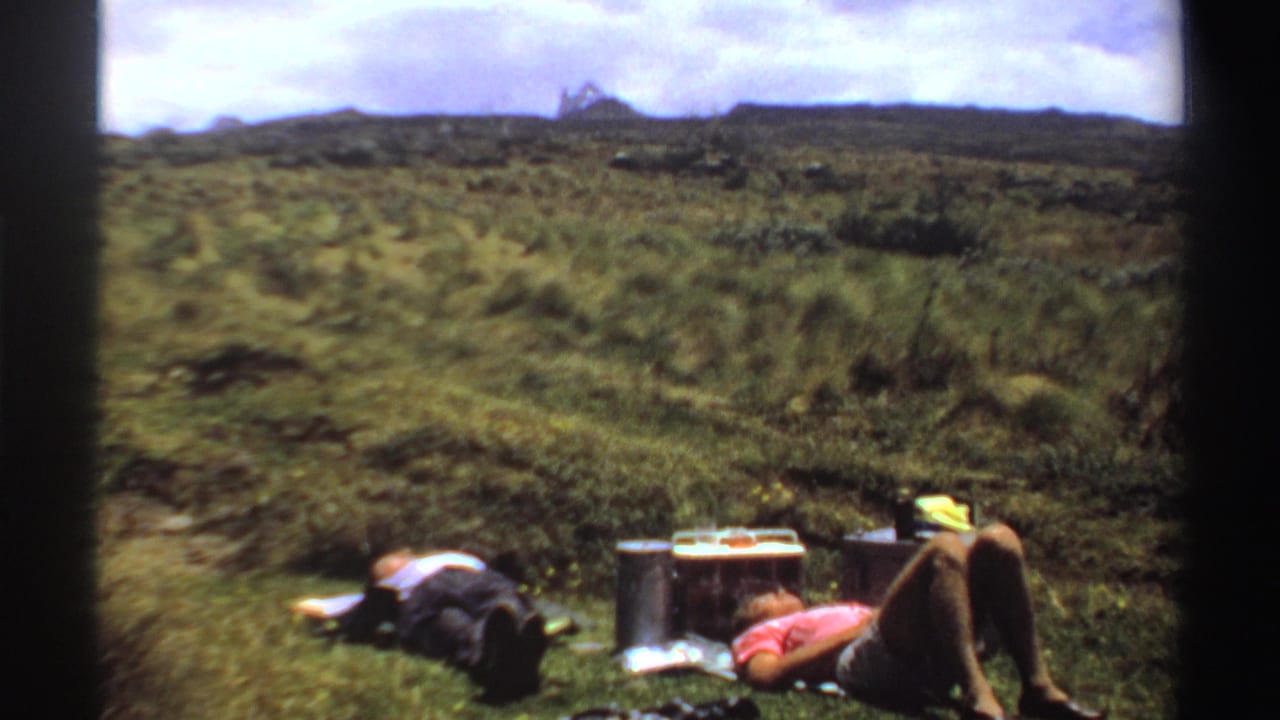Two people resting on a grassy hillside beside a cooler and supplies.