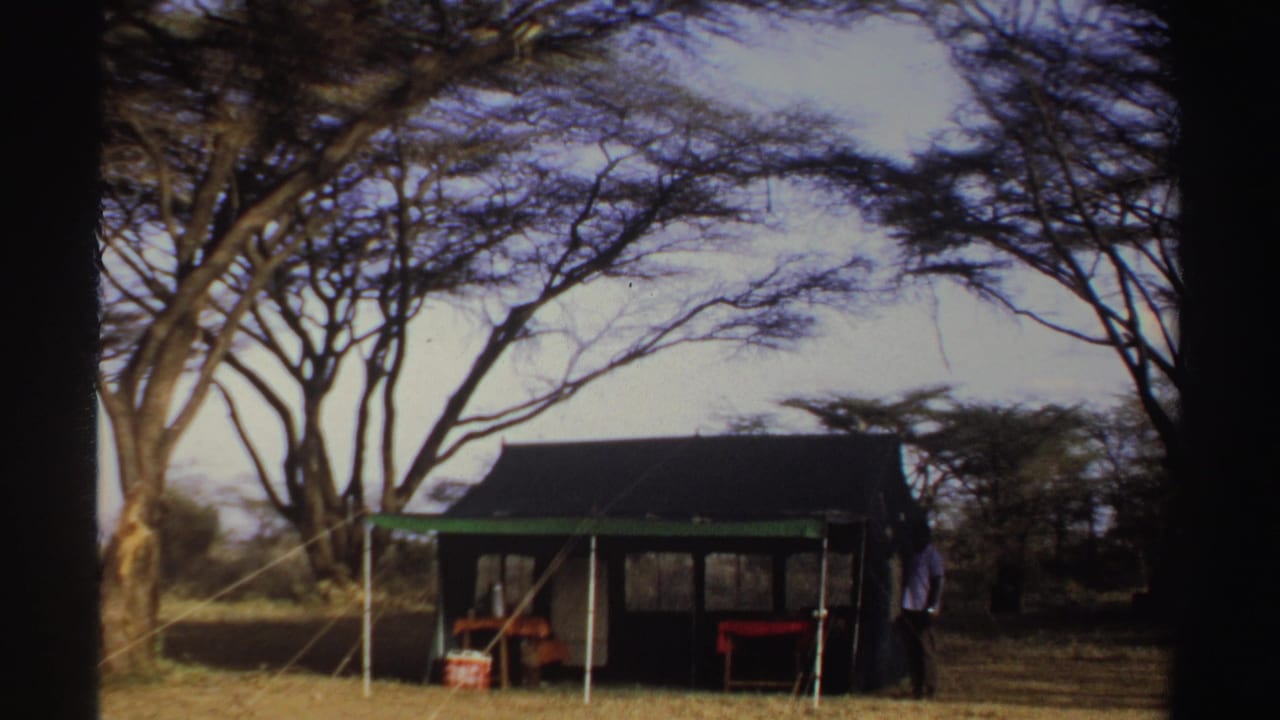 1969 Sudan home-movie frame with a camp shelter, sparse trees, dry ground, and an adult figure near the shelter.
