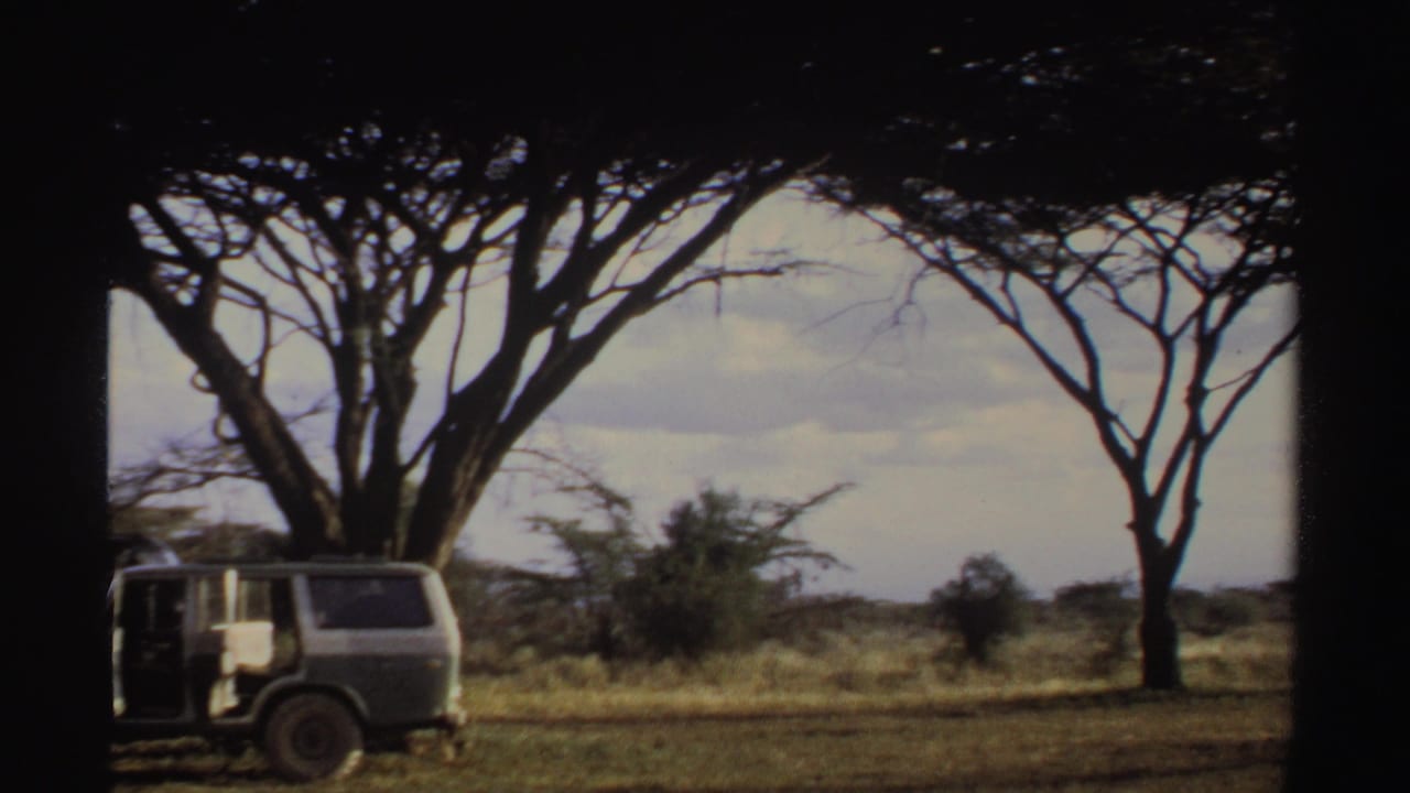 1969 Sudan 8mm frame with a parked vehicle under acacia-like trees, an open door, dry grassland, and cloudy sky.