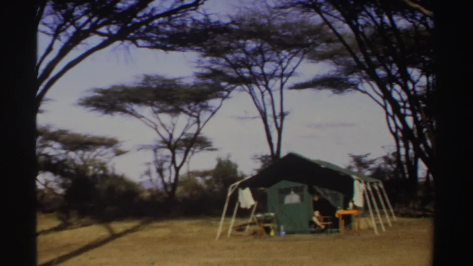 1969 Sudan home-movie frame showing a green safari-style tent under trees, with a person seated beside camp furniture.