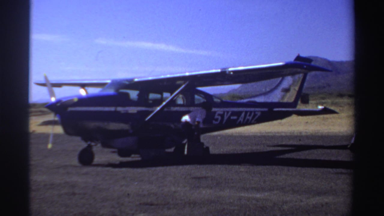 Blue and white small airplane parked on a runway with arid hills in the background.