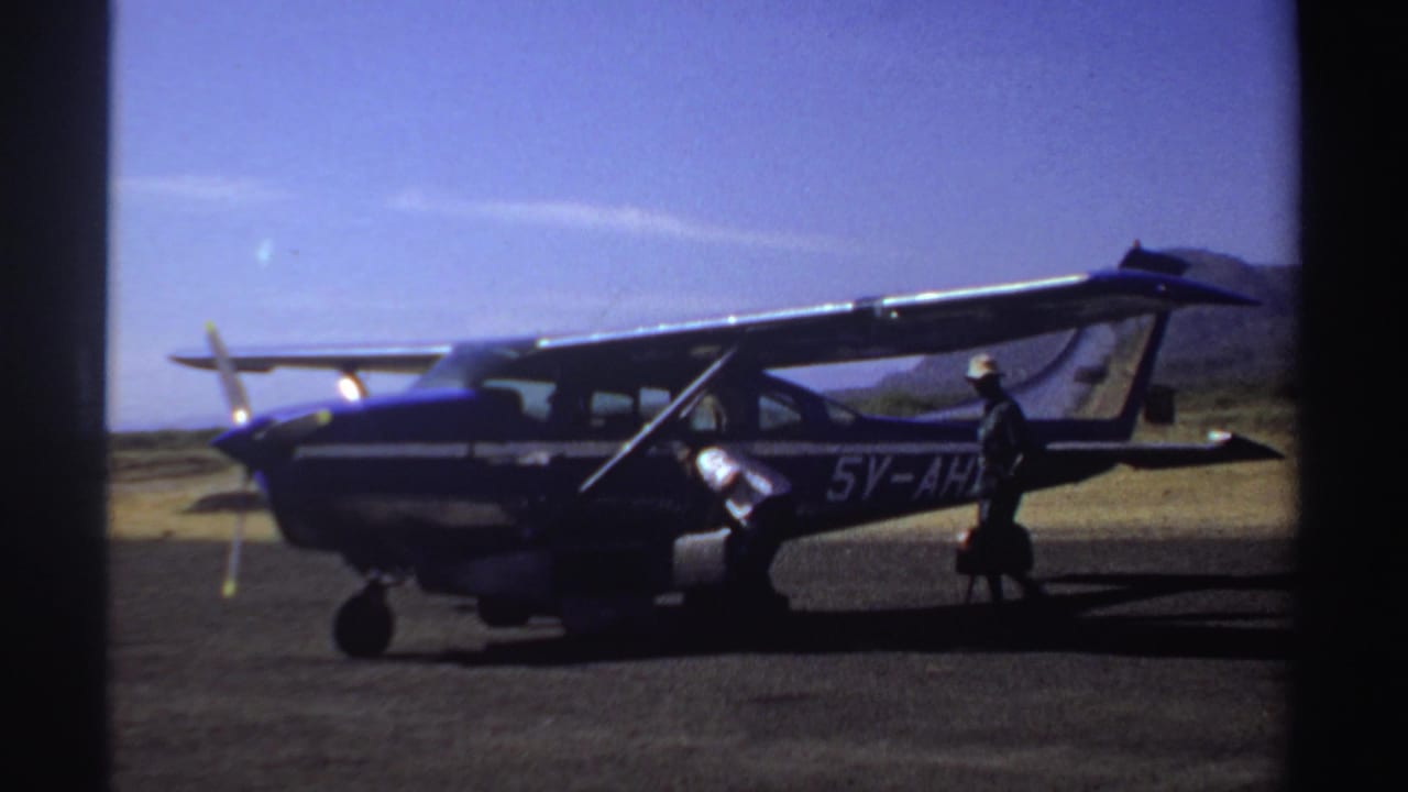 Person in a hat walks past a small aircraft while luggage sits near the door.