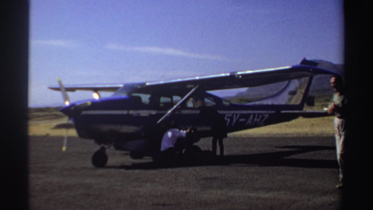 Small single-propeller aircraft on a tarmac with people near the open side door.