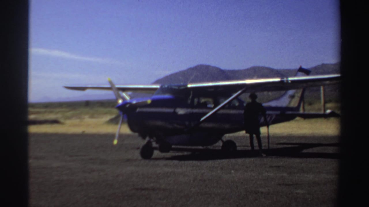 Small propeller plane remains parked on the airstrip as a silhouetted person stands near the side door.