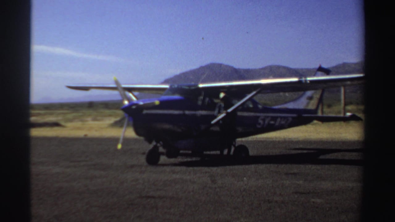 Small blue-and-white airplane parked on a remote runway with mountains in the background.