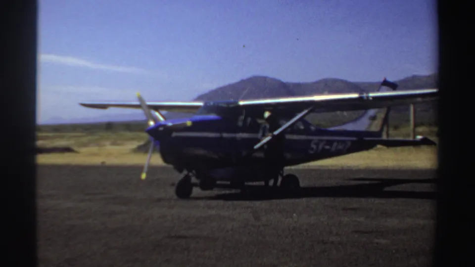 Small aircraft marked 5Y-AHZ parked on an open Sudan airstrip in 1969, with dry ground and distant mountains behind it.