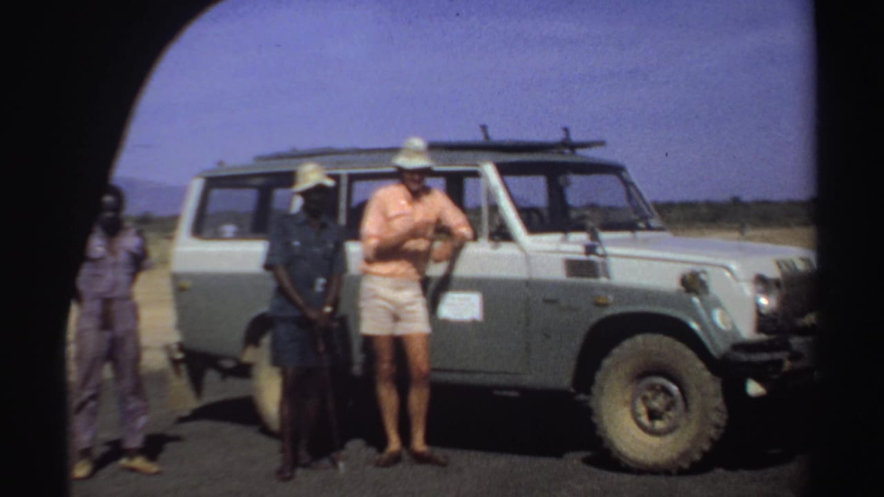 A man in shorts stands with two men beside a Land Cruiser.