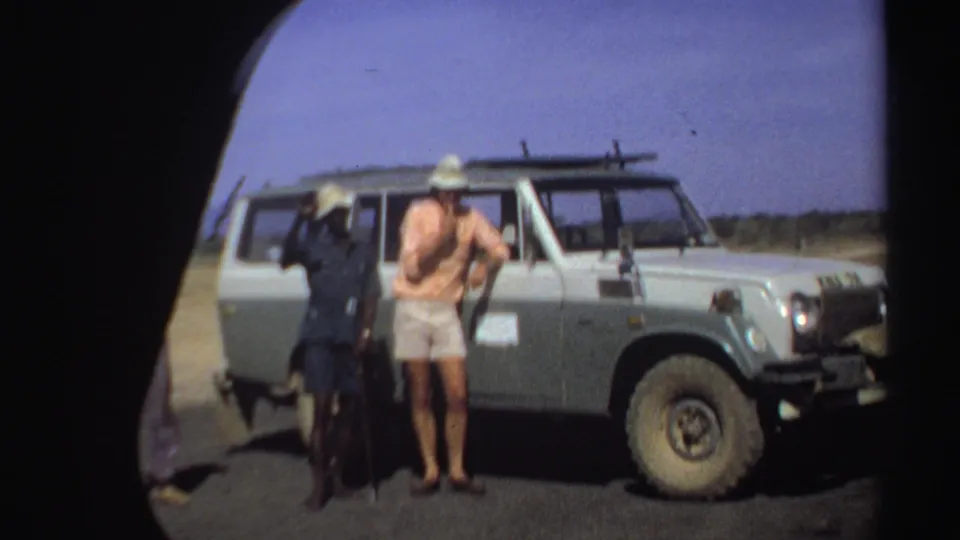 The 8mm frame shows men near a Land Cruiser during a Sudan travel stop, with soft grain and rounded frame edges.