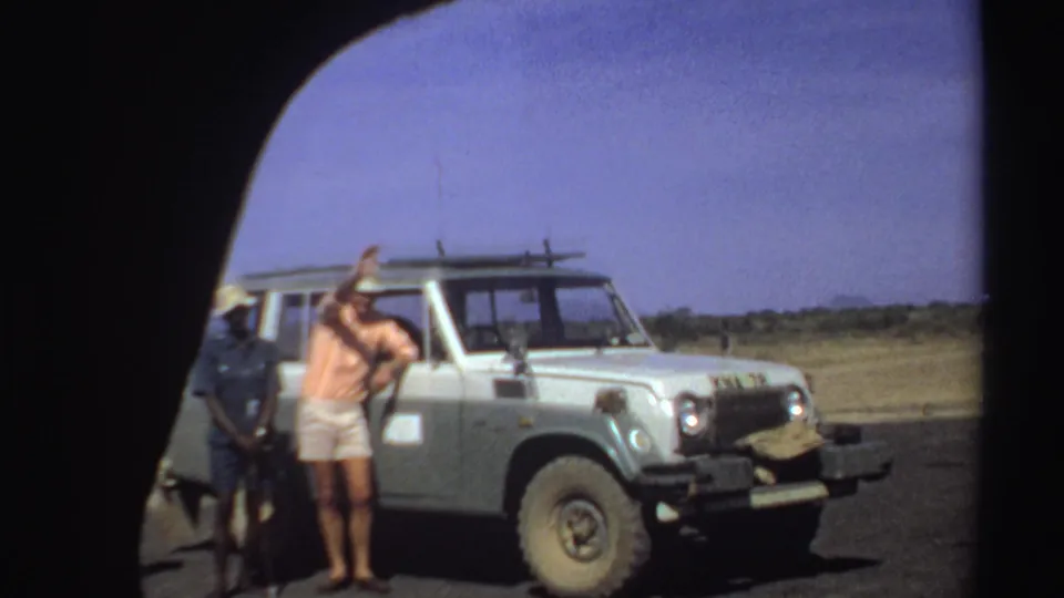 A man gestures beside the front of a Toyota Land Cruiser during a 1969 Sudan roadside safari pause.