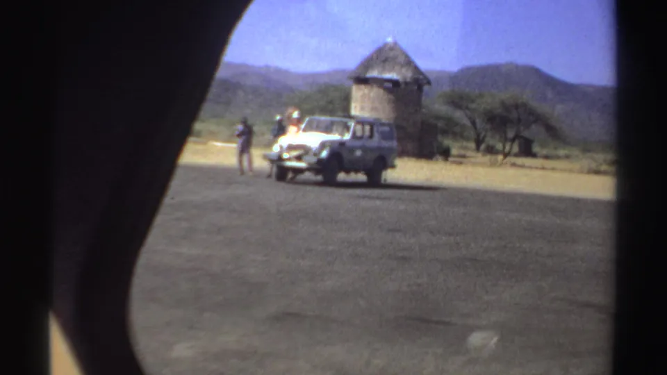Near the end of the clip, the white vehicle and people are framed beside a round thatched structure in the Sudan landscape.