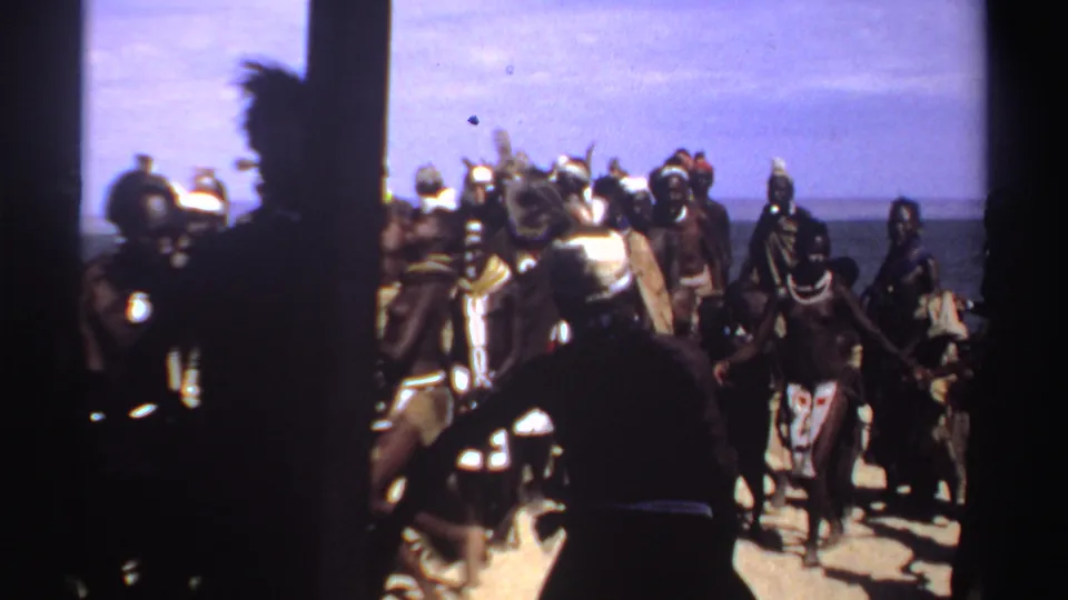 A Sudan beach gathering shows people dancing or standing in groups under a bright sky, with the sea visible beyond them.
