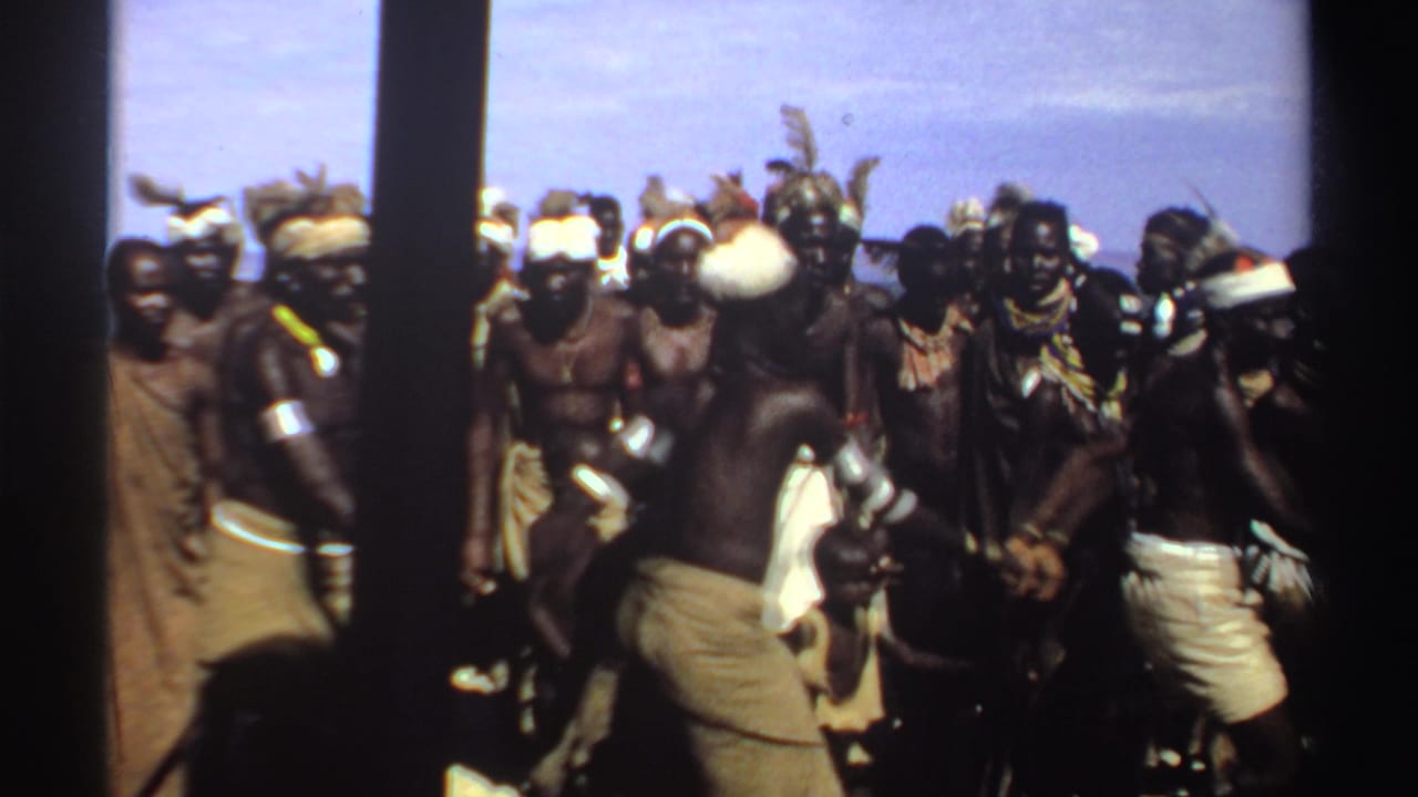 Men in headbands and wraps continue dancing in a crowded outdoor group.